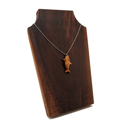 Wooden pendant necklace carved in the shape of great white shark. Made from hard maple wood. The wood shark hangs from its mouth on a black stainless steel chain against a dark walnut background.