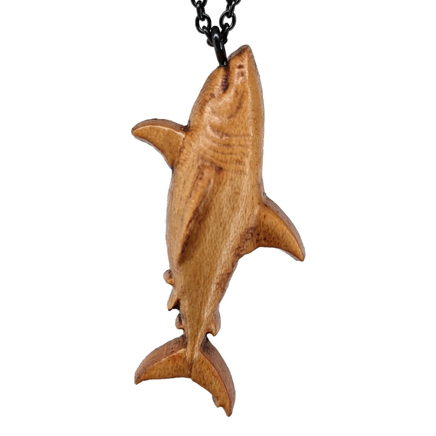 Wooden pendant necklace carved in the shape of great white shark. Made from hard maple wood. The wood shark hangs from its mouth on a black stainless steel chain against a white background.