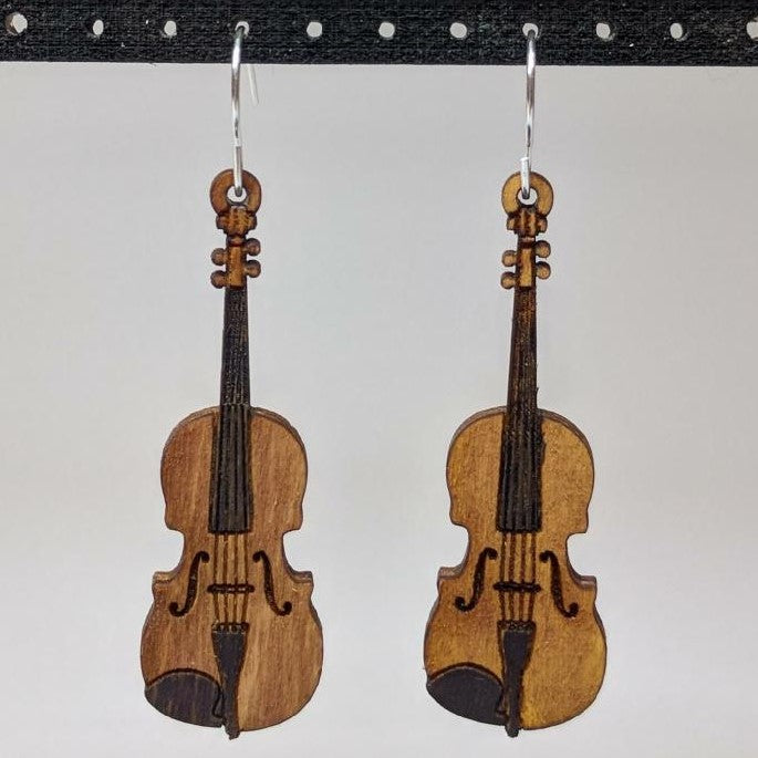 Pair of wooden earrings with silver stainless steel hooks. They are brown violins with engraved detailing and hand painted accents. Made from birch wood hanging from a model Davidson Workshop sign against a white background. (Close up View)